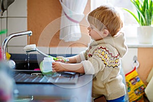 Little toddler helping in kitchen with washing dishes