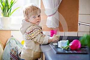 Little toddler helping in kitchen with washing dishes