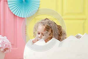 A little toddler kid is sitting in a white egg that hatched against a studio colorful background