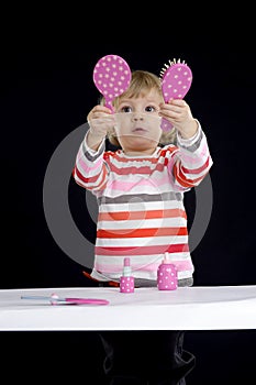 Little toddler playing with make-up toys on black
