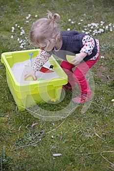 Little toddler playing with sand in the garden