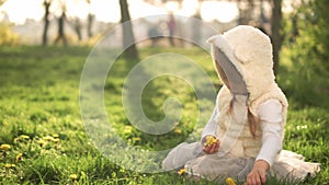 Little toddler preschool girl in dress collects yellow dandelion flowers sitting on green grass in spring park. Happy