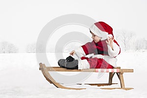 Little toddler in santa claus outfit in the snow