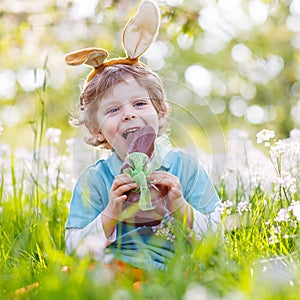Little toddler wearing Easter bunny ears and eating chocolate at