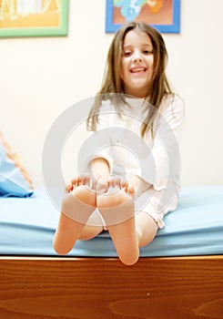 Piccola e dolce bambina di sei anni, sorride con innocenza seduta nel suo letto, che si estende i suoi piedi, che indossava il suo Pigiama.