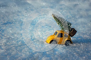 Little toy car carrying christmas trees during snowfall. Beautiful background for greeting card. Winter composition. Happy holiday