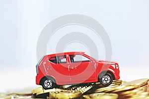 Little toy red car over a lot of money stacked coins. for bank loans costs finance.