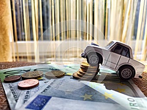 Little toy white car and euro money. Concept of the expensiveness of buying a new car, affordability of buying an old