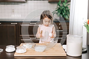 Little two-year-old girl is learning to bake cake standing breaking eggs