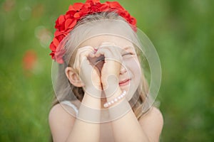 little ukrainian girl looking through heart gesture made with hands in summer green park. Gesture of love to Ukraine by pretty