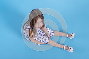 A  little upset girl with long blonde hair sits on blue background in studio, top view