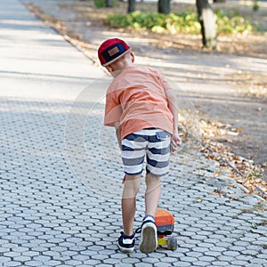 Little urban boy with a penny skateboard. Kid skating in a summer park. City style. Urban kids.