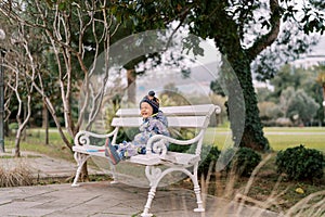 Little whimpering girl in overalls sits on a park bench