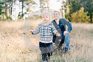 Little whimpering girl walks across the lawn from a smiling dad