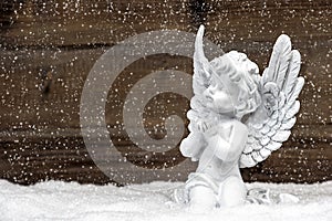 Little white angel on wooden background in snow