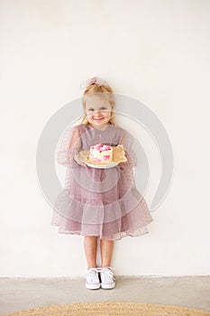 Little white Birthday girl with cake in a pink dress laughs. Preschooler.