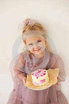 Little white Birthday girl with cake in a pink dress laughs. Preschooler.