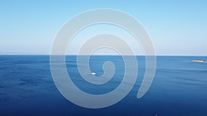 Little white boat sails towards coast on open sea. Boating in the tropics. Aerial view