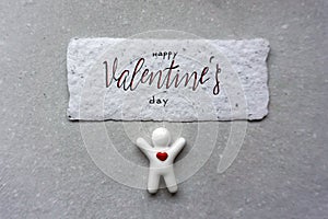 Little white man with heart and valentine card on gray paper background