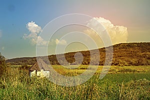 Little white old rural house surrounded by a sunny landscape, summer fresh vital day, hill covered with green grass and huge cloud