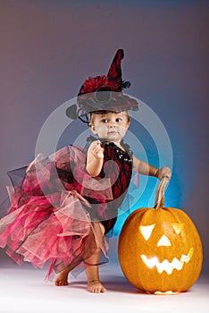 Little witch girl child laughing among pumpkins and candles