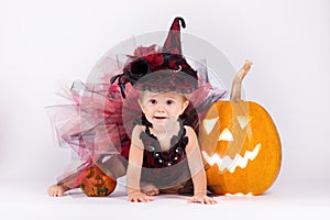 Little witch girl child laughing among pumpkins and candles on a white background.