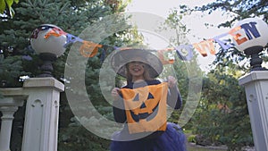 Little witch holds Trick or Treat bag, asks for sweets outdoors, Halloween party