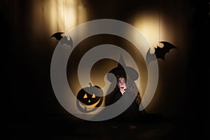 Little witch sits and is afraid of shadows in the form of pumpkin and bat. Halloween holidays concept