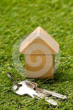 Little wooden miniature house model on green grass background with house keys - ecological living or house building concept