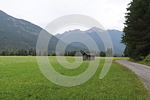 little wooden mountain shed in a pastural meadow surrounded by mountains