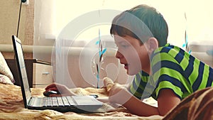 Little young boy using a notebook in a bedroom are playing the bed. boy teen social media internet on a laptop indoors