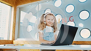 Little young cute girl using laptop to working or playing games. Erudition.