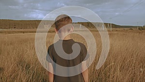 Little young dreamy boy walking in the picteresque field beautiful landscape yellow grass