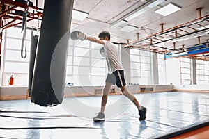 Little young fighter using punching bag during taining