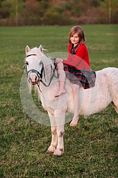 Little young girl in dress sitting on a pony riding Lady