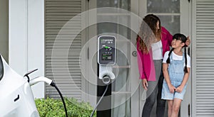 Little young girl help her mother recharge EV car at home. Synchronos