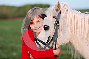 Little young girl in a red dress hugging his head a white horse