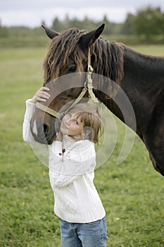 Little young girl in a white pullover and jeans hugged his head to horse's on farm warm autumn day. Lifestyle portrait