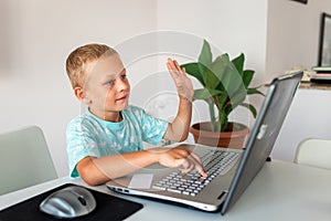 Little young school boy working at home with a laptop and class notes studying in a virtual class