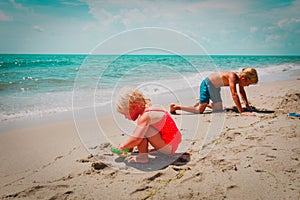 Littlegirl and boy play with sand on beach