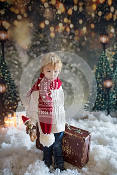 Littlw toddler child with suitcase and little gingerman toy in hand, walking in a snowy forest, christmas picture