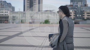 Live camera follows man walking on city square in slow motion looking around. Panning shot side view of successful