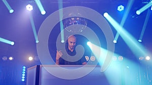 Live DJ performance of energetic bald man with headphones, dancing on party concert musician stage