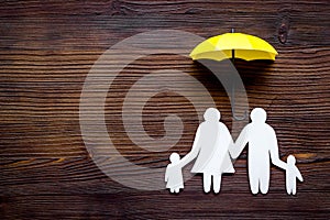 Live insurance concept. Family silhouette protected by umbrella on dark wooden background top-down copy space