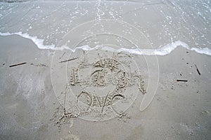 Live Laugh Love phrase written on the beach in the sand as the ocean waves roll in