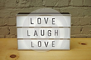 Live Laugh Love word in light box on white brick wall background