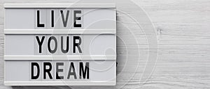 `Live your dream` words on a lightbox on a white wooden background, top view. Overhead, from above, flat lay. Space for text