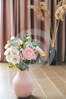 A lively bouquet of assorted flowers brightens the room, housed in a textured pink vase on a wooden floor against the backdrop of