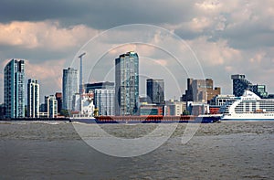 Liverpool city skyline looking across the river Mersey with large cargo vessel passing upstream