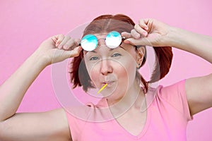 Living on bright side of life: portrait of beautiful woman in pink shirt with pigtails hairstyle, blue sunglasses and lollipop